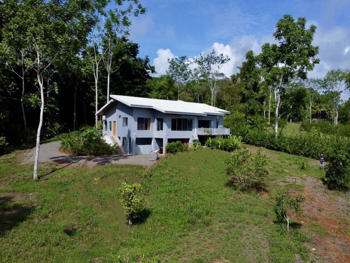 |Modern living room with minimalist furniture and natural light |Property borders tropical forest with walking trails|Bright bathroom with large mirror and tile accents |Porch with seating and views of forest and gardens |Bathroom with modern finishes and neutral colors |Panoramic ocean view from hillside home in Agujas |Large living area with tropical decor and natural light |Covered patio with seating and tropical landscaping|Small forest creek flowing along property edge||Patio overlooking Golfo Dulce and tropical forest |Rolling tropical hills with ocean backdrop|Elevated deck overlooking Golfo Dulce and hills|Bedroom overlooking Golfo Dulce in Agujas Costa Rica|Mango